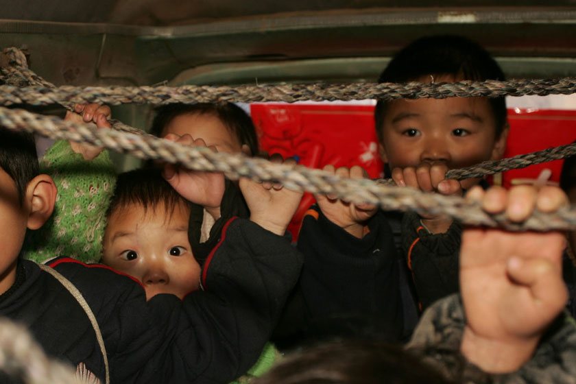 2006年11月28日，郑州，一辆装了16个孩子的松花江面包车查扣。这辆面包车车身多处掉漆，左边车门关不紧，车内原先的座位已被拆掉，摆放了5个木制小板凳，车顶绑了两根棉绳，四五位年龄稍大的孩子一手拉着绳子，一手扶着车窗。 赵克/CFP_特辑：危险的“校车”