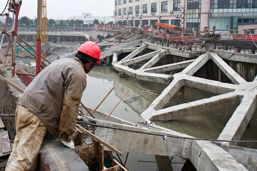2012年2月29日，上海市松江区，一位工人站在工地上朝坍塌的地方看去。 孙湛/CFP_上海松江工业园区路面大面积塌陷