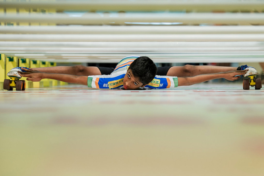 2012年7月25日，11岁印度男孩可凯恩在香港表演脚踩旱冰鞋从一排离地面不到18厘米的杆子下穿过。这项活动在一家商场内举行，旨在鼓励老人积极投身于运动。 PHILIPPE LOPEZ/东方IC_财新每周图片(2012.7.21-7.27)