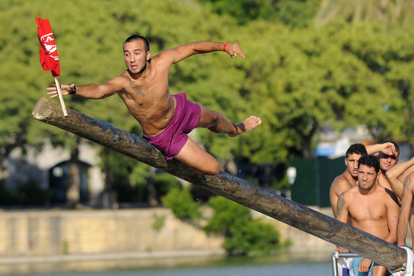 2012年7月22日，西班牙塞维利亚，嘉达琪维尔河上正在举办传统的爬杆活动。男人们站在木杆上，拿到顶部的旗子才算胜利。 CRISTINA QUICLER/东方IC_财新每周图片(2012.7.21-7.27)