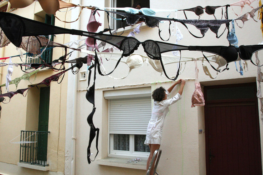 2012年7月20日，法国巴纽尔斯，一名妇女悬挂胸罩。这一自发的公民行动是当地妇女Barbara Frenz发起的，她打算跟其她妇女一起在楼与楼之间拉起一条条用胸罩连起来的装饰链条，抗议一项私人码头项目，呼吁建设生态友好型港口。 RAYMOND ROIG/东方IC_财新每周图片(2012.7.21-7.27)