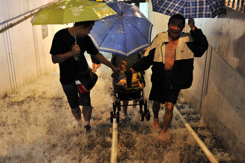 2012年7月21日，北京西站附近的地下通道涌入大量雨水，三位行人抬着婴儿车经过。李文/新华社_北京逝者