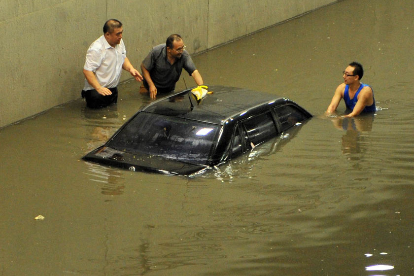 2012年7月21日，北京西站附近的桥下积水，三位男士将被淹的汽车推出积水。新华社_北京逝者
