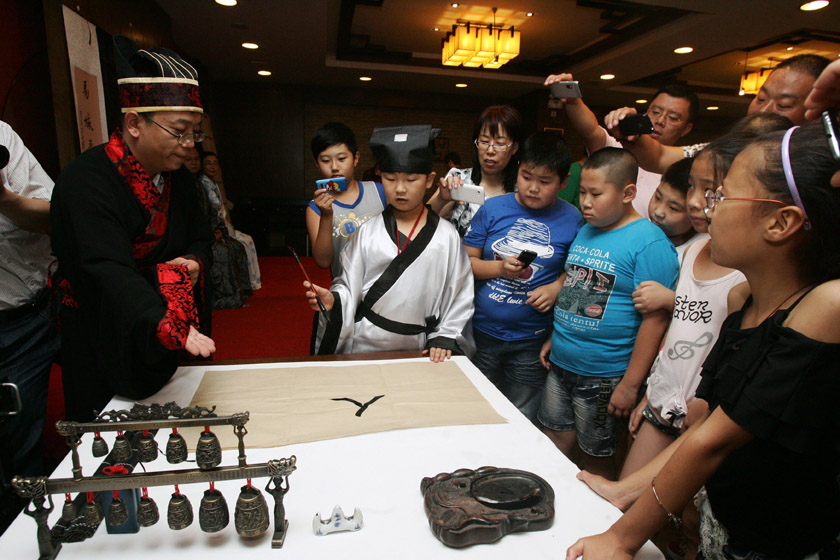 7月30日，太原，成童礼上的“启蒙开笔”，孩子们在父母的帮助下，认真地在孔子面前写下一个端正的人字。从此后就要开始学习做人，刻苦读书。 张云/中新社山西分社_太原儿童举行“成童礼”