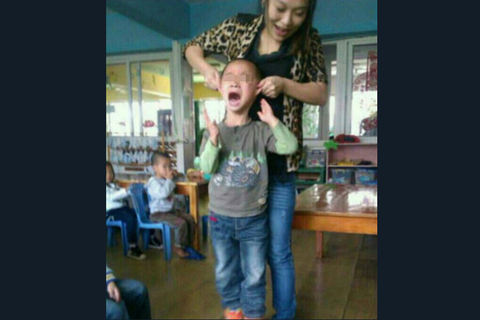 截屏图：女教师颜某揪住一位男童的耳朵向上提离地面，并让同事拍照留念。