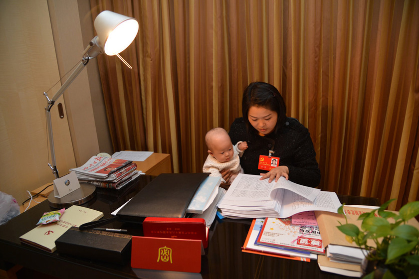 11月10日晚，北京，罗玮参加完四川团的会议，回到驻地房间继续阅读学习大会的有关材料，把已有睡意的女儿斜抱在怀中。
 尹钢/CFP_四川两位女代表携婴儿参加十八大