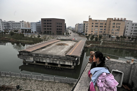 浙江温州龙湾区状元街道石坦村有座“断桥”，主桥在河面建了大部分后停工，剩下一个断口，距今五年多时间不见进展，无人问津。据悉，在大桥施工时，有几名拆迁户因对拆迁政策不满开始阻挠施工，后经多次协商未果，以至于施工受阻，拖延至今。图为2月20日，住在岸边的董女士在阳台收衣服，她希望这桥能早日联通给村民带来方便    魏一晓/CFP