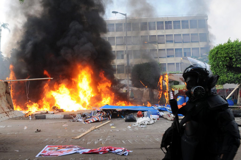 epa03824001 Smoke rises as a tent burns at one of the two sites of the sit-in by the Egyptians supporting ousted president Morsi (depicted in poster)