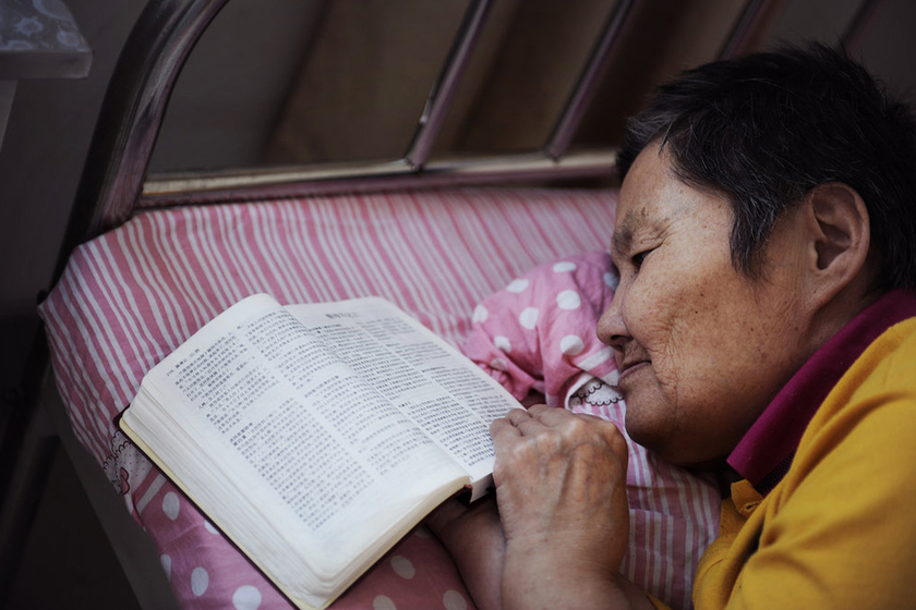 2013年6月28日，黑龙江佳木斯，张慧颖在床头放了本《圣经》，她一躺下就拿出来看，可是她已经不认识上面的字。张慧颖，64岁，北京知青。1966年下乡到291农场，后嫁给农场的一名知青，育有一女。婚后因感情问题而致精神分裂，甚至觉得曾经一起下乡的北京知青现在都还在。患病后家属不肯接受她，她再也没有回过北京。   孙俊彬/CFP_走不出的北大荒