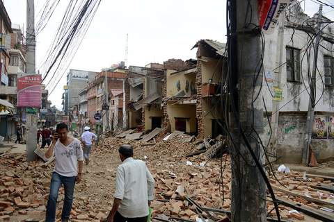 Nepalese people walk past collapsed buildings at Lalitpur