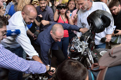 Outgoing Greek Finance Minister Yanis Varoufakis (C) helps lift a motorcycle that fell on the ground as journalists surrounded him while he was leaving the finance ministry in Athens on July 6