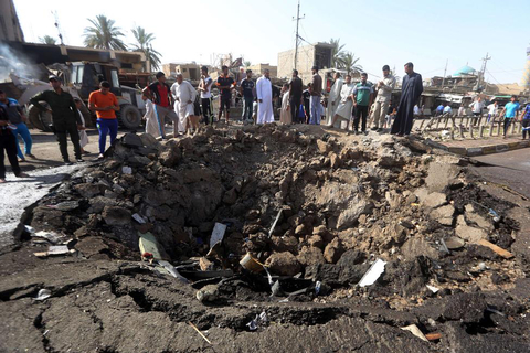 Iraqi men look at a crater left by a massive suicide car bomb attack carried out the previous day by the Islamic State group in the predominantly Shiite town of Khan Bani Saad