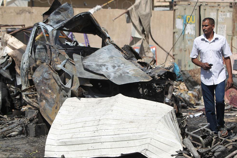 An Iraqi man walks past the wreckage of cars in the aftermath of a massive suicide car bomb attack carried out by the Islamic State group in the predominantly Shiite town of Khan Bani Saad