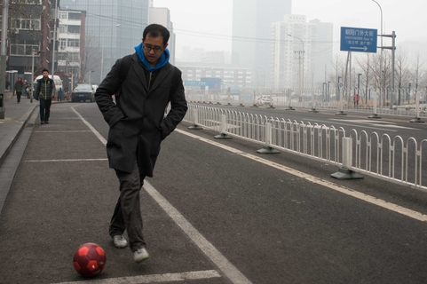 2015年12月8日，北京，景华北街，一名上班族踢球上班以保持自己的“脚感”。雾霾天气里，即便中小学生停课，选择在进行踢球或打篮球等户外运动的人依然很少。 韦毅/财新视觉中心实习生