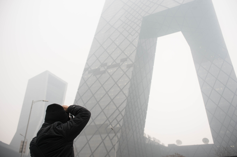 2015年12月8日，北京，东三环，一名行人在给雾霾中的中央电视台总部大楼拍照。 韦毅/财新视觉中心实习生