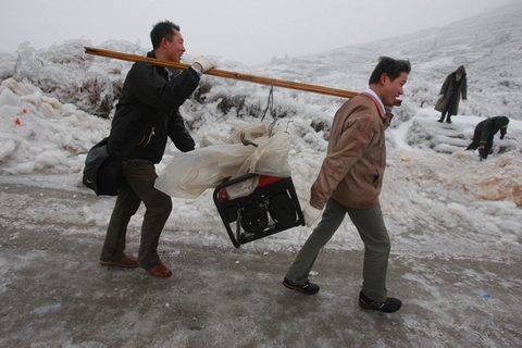 2008年2月2日,坪乳公路上,深圳打工的陈先生(左)与老乡用木棍抬着一台