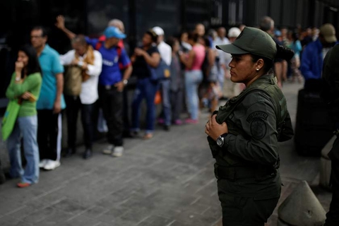 A Venezuelan soldier stands guard as people line up to get into a Banco Mercantil branch in Caracas