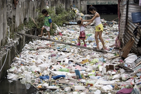 当地时间2018年1月17日，菲律宾首都马尼拉，当地居民在木板做的小桥上准备过河，他们脚下的河道漂满了垃圾。图/视觉中国