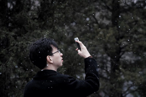 2018年3月17日，北京团结湖，市民举起手机拍摄落雪景观。3月17日，北京大部地区出现雨雪天气。截至3月16日，北京南郊观象台连续无有效降水日数已经达145天，这场雨雪结束了连续无有效降水日数最长纪录。 图/财新记者 梁莹菲