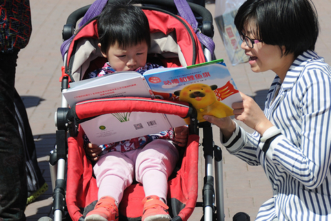 2016年4月17日，北京，在朝阳公园举行的2016年北京书市迎来客流高峰。一名母亲指导坐在婴儿车内的孩子看书。图/视觉中国
