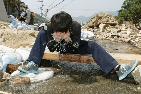 当地时间2018年7月18日，日本广岛县吴市，暴雨灾区志愿者洗脸。暴雨过后，日本多地又迎来高温天气。由于罕见高温的袭击，军队和志愿者们在灾区的救援和恢复工作也遭遇了阻碍。据英国《独立报》报道，上周末以来，这股强烈的热浪横扫日本，已造成14人死亡，上千人在医院接受中暑治疗。图/视觉中国