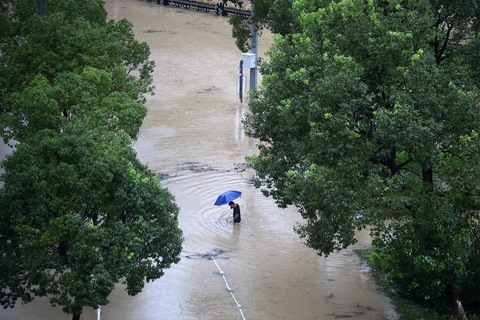 2019年8月10日，浙江温岭，温岭市太平街道上，一名行人横穿积水严重的马路。“利奇马”带来的强降水导致温岭市太平街道多个小区被淹，积水最深处近2米，上千居民生活受到影响。图/新华社