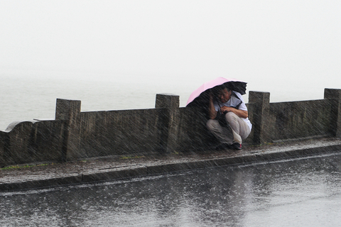 2019年8月9日，浙江杭州，受超强台风 “利奇马”影响，西湖断桥突降暴雨，一名男子蹲在护栏边躲避风雨。图/视觉中国